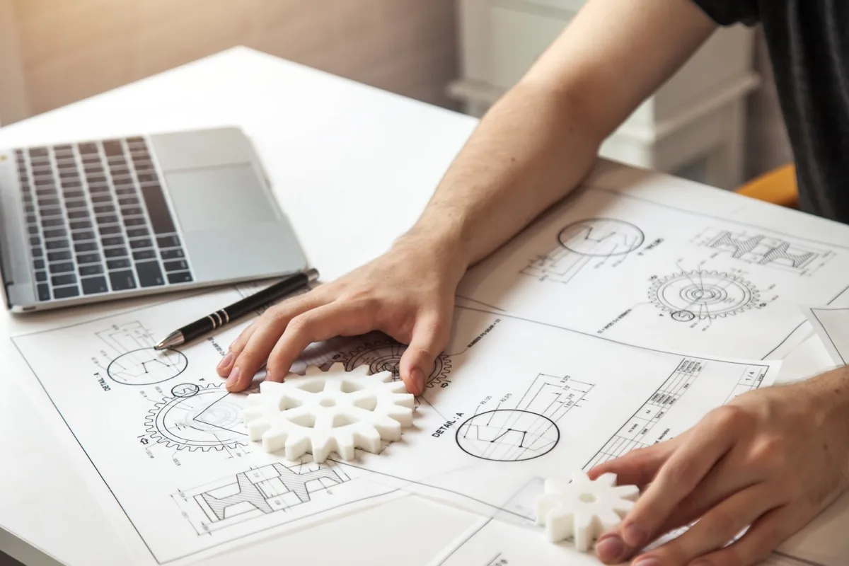 An employee working with gears and blueprints, illustrating first principles thinking in a performance review framework.