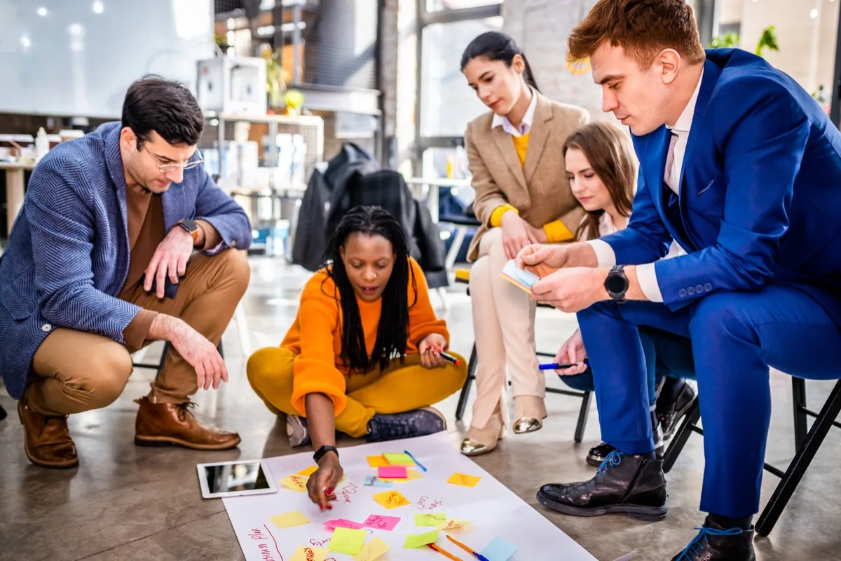 A diverse team collaborating in an office workshop using sticky notes on the floor.